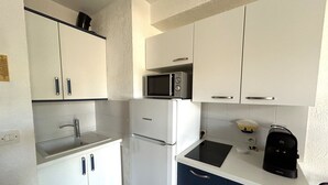 Una cucina compatta con mobili bianchi, un forno a microonde, un frigorifero e una macchina per il caffè.