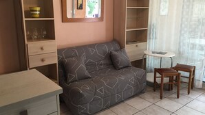 A cozy living area with a sofa, a small table, and two chairs. There is a bookshelf with a mirror above it. - Ground Floor with Private Parking for 4 (Argelès-sur-Mer)