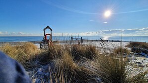 A beach with a wooden walkway leading to a structure, a fence, and the ocean in the background. - Apartment with Sea View, Sauna, and High-Quality Furnishings (Sierksdorf)