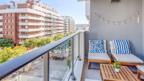 A balcony with a seating area, a view of adjacent buildings, and a string of lights. - Charming Modern Apartment in Estepona (Estepona)