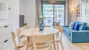 A modern living room with a round wooden table, blue sofa, and a balcony with a view of buildings. - Charming Modern Apartment in Estepona (Estepona)