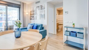 A modern living room with a round wooden table, blue sofa, and a view of the city through large windows. - Charming Modern Apartment in Estepona (Estepona)