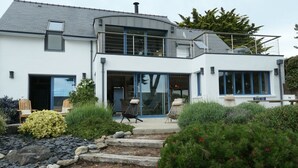Una moderna casa a due piani con un'ampia porta d'ingresso in vetro, area salotto esterna e un giardino curato.