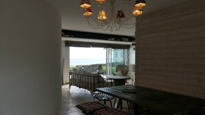Zona pranzo con vista sul mare, un tavolo in legno, panche e un lampadario.