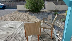 Een terras met een houten dek en twee rieten stoelen.