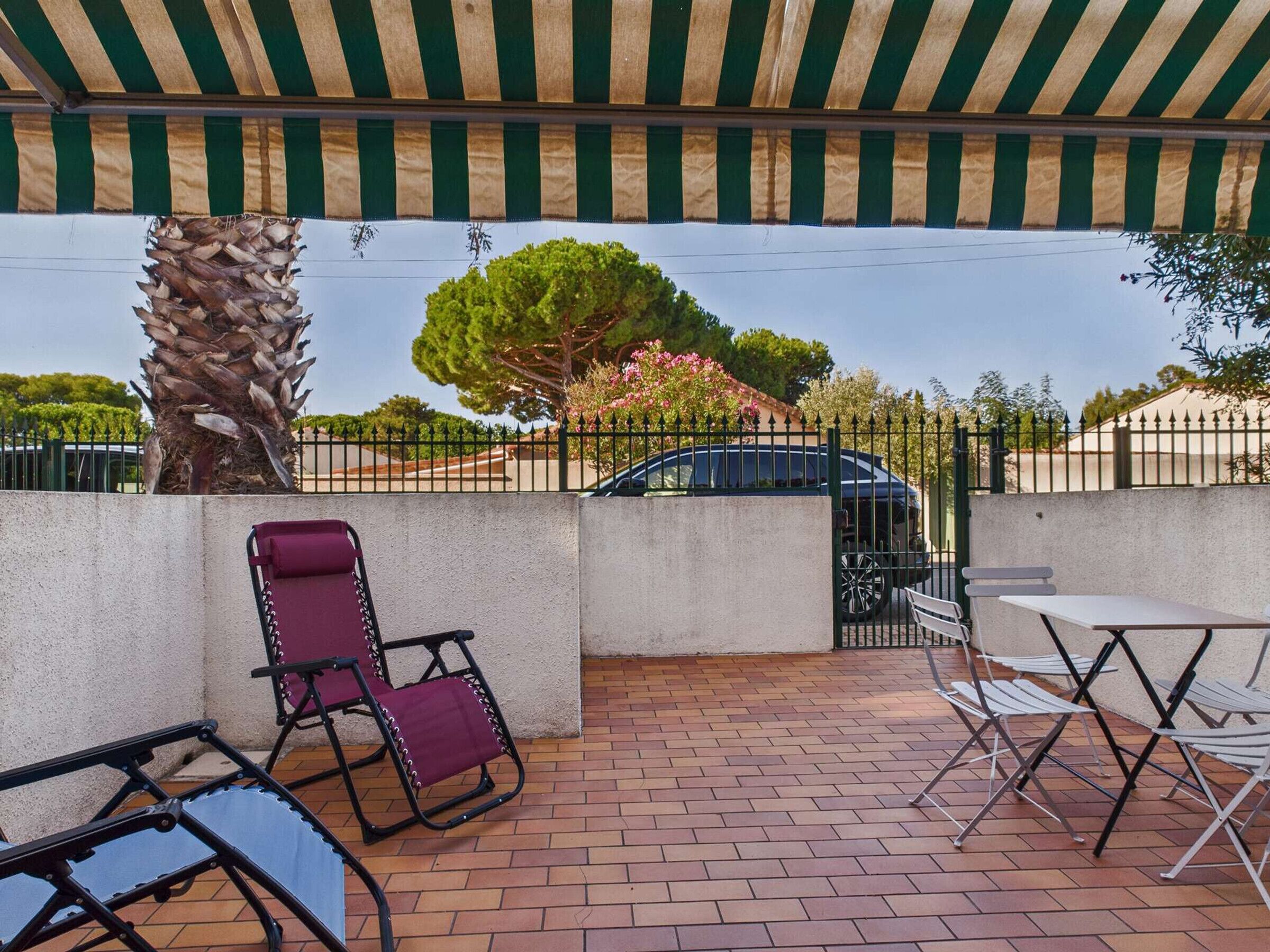 Un patio al aire libre con un toldo a rayas, una palmera y un coche estacionado al fondo.