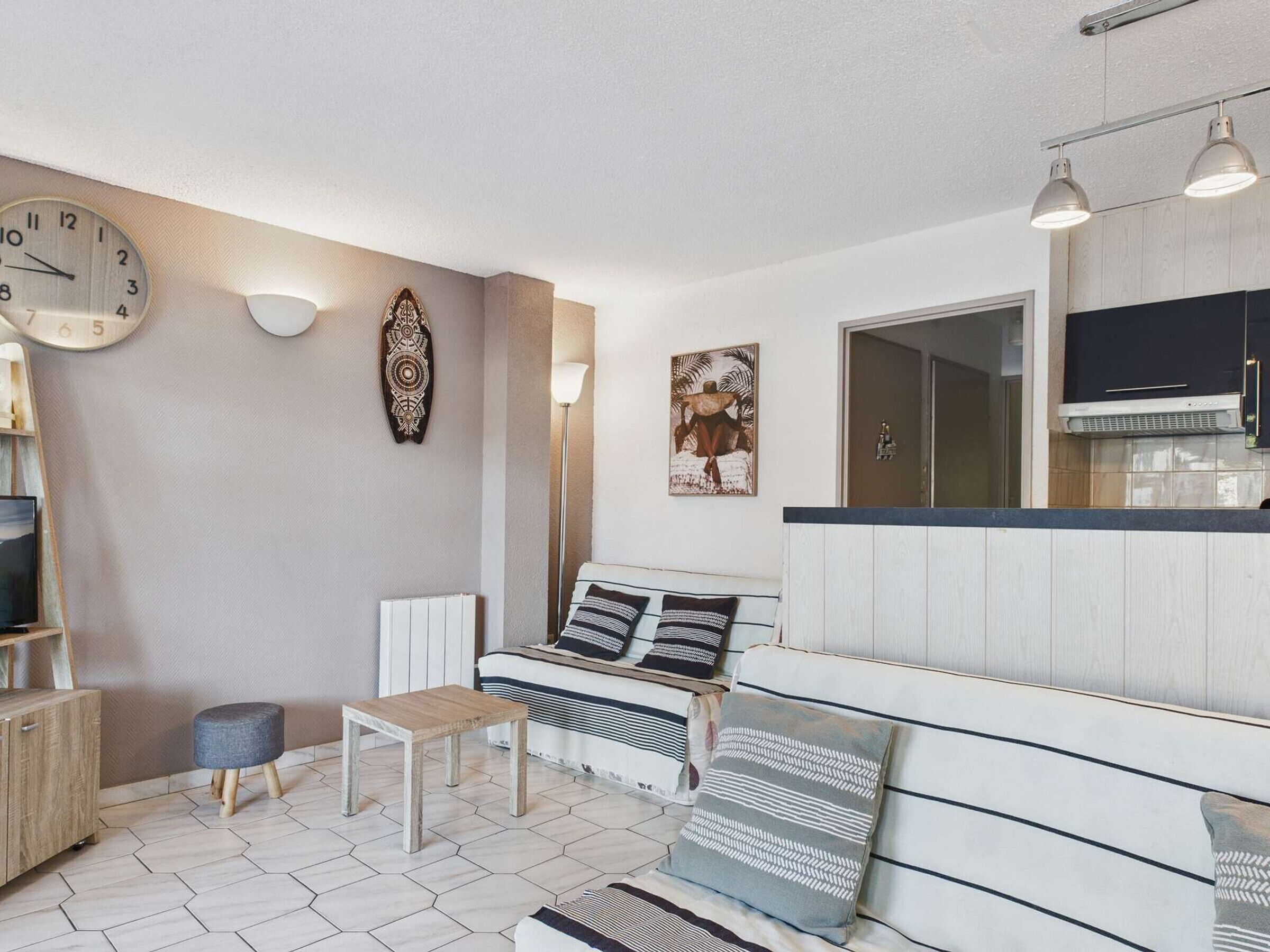 Een moderne woonkamer met een bank, salontafel en televisie. Er is een keuken met kastjes en een fornuis.