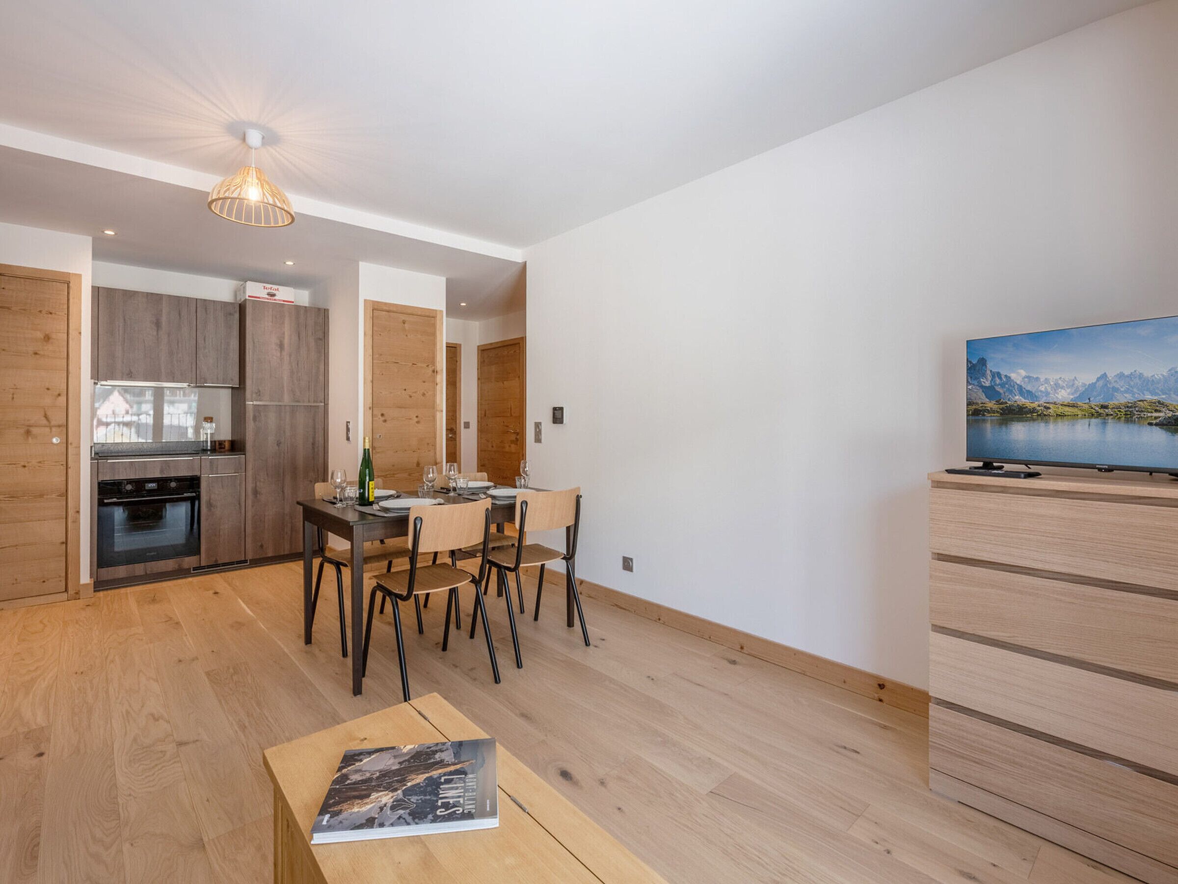Una sala de estar moderna con comedor, armarios de madera, un televisor y vistas a montañas.