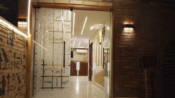 A hotel lobby with a modern design, featuring a glass partition with Egyptian hieroglyphs, a polished marble floor, and a brick wall on the right. - ش ابو الهول السياحى (giza)