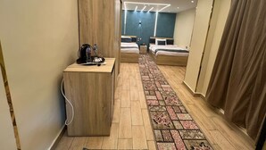 A modern hotel room with a wooden wardrobe, a desk with a water bottle, two beds with headboards, a patterned rug, and a blue accent wall. - ش ابو الهول السياحى (giza)