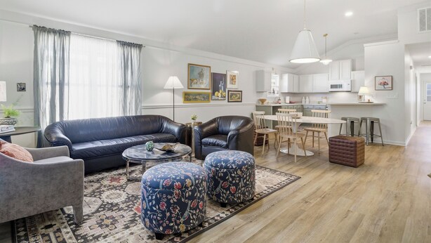 Ett modernt vardagsrum med en svart lädersoffa, två matchande sittpallar, ett runt soffbord och en matplats med ett vitt bord och stolar.