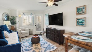 Een woonkamer met een bank, fauteuil, eettafel en een plafondventilator.