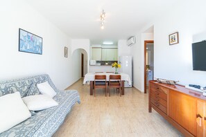 Un salon avec un canapé, une table à manger entourée de chaises, un buffet en bois et, au fond, une cuisine.