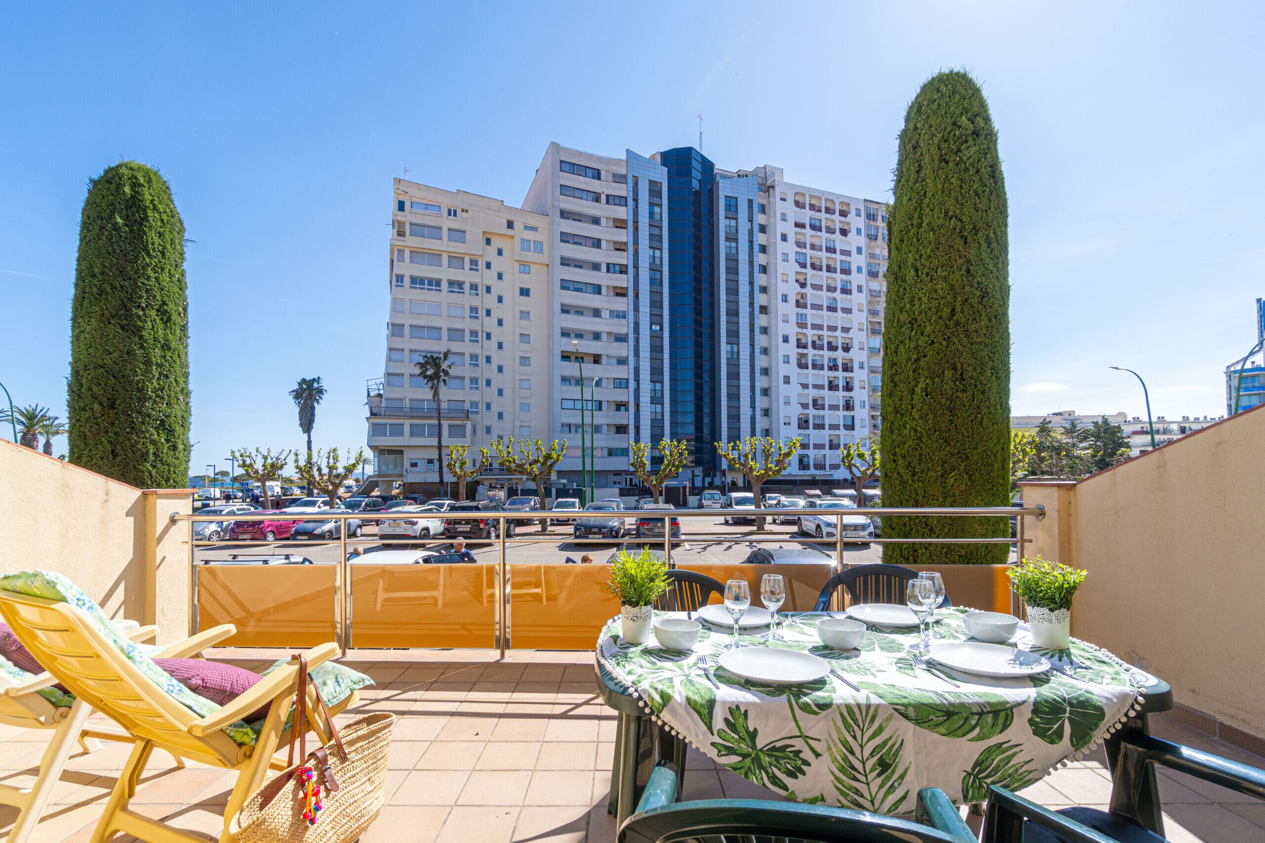 A rooftop terrace with a dining table set for two, lounge chairs, and a view of a tall building in the background.