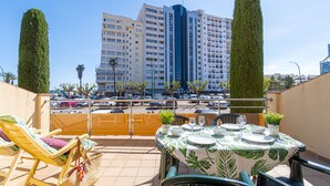 A rooftop terrace with a dining table set for two, lounge chairs, and a view of a tall building in the background. - 0088-MIRABLAU Apartment with side views of the beach (Empuriabrava)