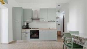 Une cuisine moderne avec des meubles de couleur vert clair, un four encastré et un coin repas comprenant une table et des chaises.