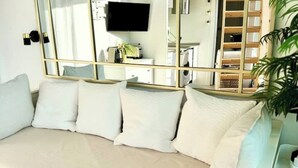 A modern bedroom with a beige sofa, a large mirror, a flat-screen TV, and a plant. - Studio with Mezzanine and Private Terrace in Parque Retiro (Madrid)