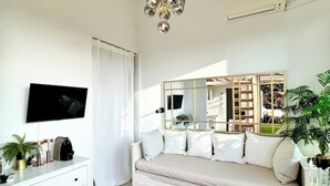 A modern bedroom with a white sofa, a large mirror, a flat-screen TV, and a white dresser. - Studio with Mezzanine and Private Terrace in Parque Retiro (Madrid)