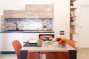 Una cocina moderna con una mesa de madera, sillas anaranjadas, una cafetera y un bol de fruta.