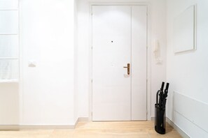 Eine weiße Tür mit goldener Klinke, ein schwarzer Regenschirmständer und ein gerahmtes Bild an der Wand.
