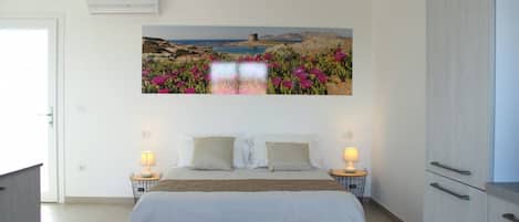 A bedroom with a bed, bedside tables, a wall-mounted air conditioner, and a painting of a landscape.