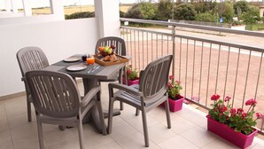 A balcony with a table set for breakfast, including croissants, fruit, and juice. There are four chairs around the table and potted plants on the floor. - Spacious 40 square meter apartment with independent access via magnetic card. The accommodation includes a fully equipped kitchenette, a living room with a comfortable sofa bed for two, a bedroom with a double bed, and a private bathroom with a shower an (Stintino)