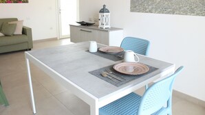A dining area with a table set for two, a green sofa, and a small kitchen area with a lantern. - Spacious 40 square meter apartment with independent access via magnetic card. The accommodation includes a fully equipped kitchenette, a living room with a comfortable sofa bed for two, a bedroom with a double bed, and a private bathroom with a shower an (Stintino)