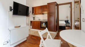 Cocina compacta con armarios de madera, horno integrado y televisor de pantalla plana en la pared.