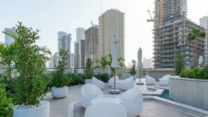 Een terras op het dak met moderne zitplaatsen, potplanten en uitzicht op omliggende hoogbouw.