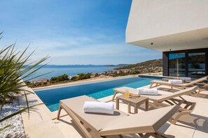 A modern pool area with lounge chairs and a view of the sea. - Villa Oliva Zadarvillas (Primosten)