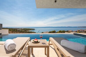 A poolside view with a table, a glass of red wine, and a slice of watermelon. - Villa Oliva Zadarvillas (Primosten)