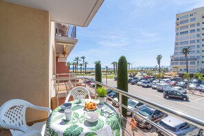 Ein Balkon mit Tisch für zwei Personen, einem Blumentopf und Blick auf einen Parkplatz sowie Gebäude.