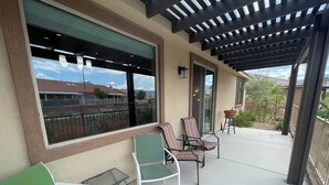 Un patio couvert avec un espace salon extérieur, comprenant des chaises et une table, et offrant une vue sur le quartier environnant.