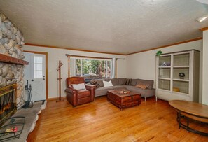 Ein Wohnzimmer mit Kamin aus Stein, einem Ledersessel, einer Couch, einem Holztisch und einer Vitrine mit Glastüren.