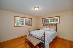 Ein Schlafzimmer mit einem hölzernen Bett, einer Bank, zwei Fenstern und einer Deckenleuchte.