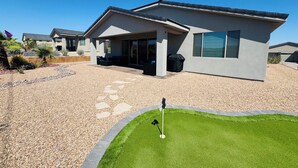 Une maison moderne dotée d’un patio couvert, d’une pelouse et d’un espace dédié à l’entraînement au golf.