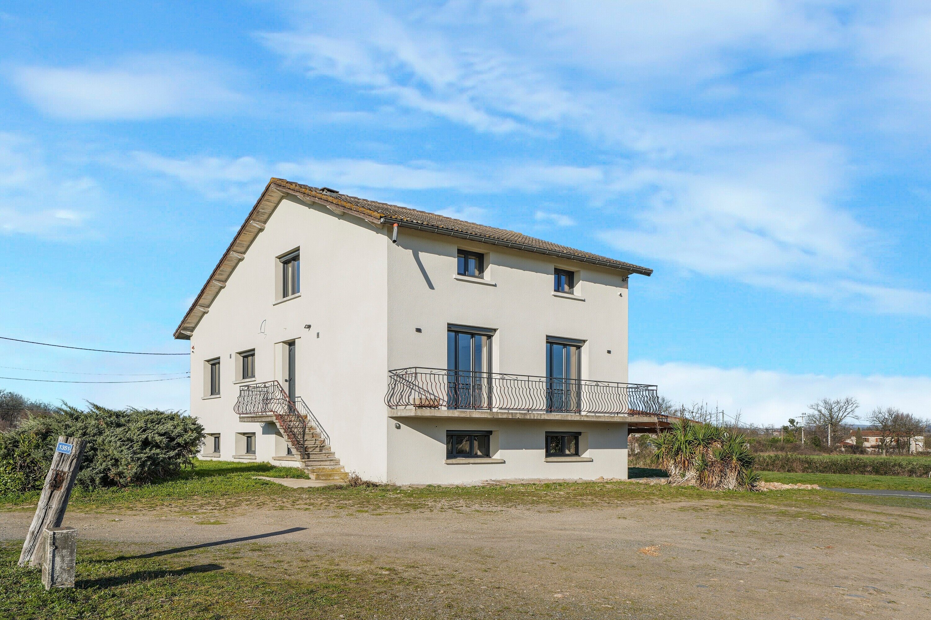 Ein zweistöckiges Gebäude mit Balkon, Treppe und kleinem Garten.