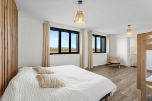 Un dormitorio con una cama grande, dos ventanas, una silla y una puerta de madera.