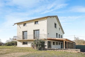 Una casa de dos pisos con balcón, porche cubierto y cimientos de piedra.