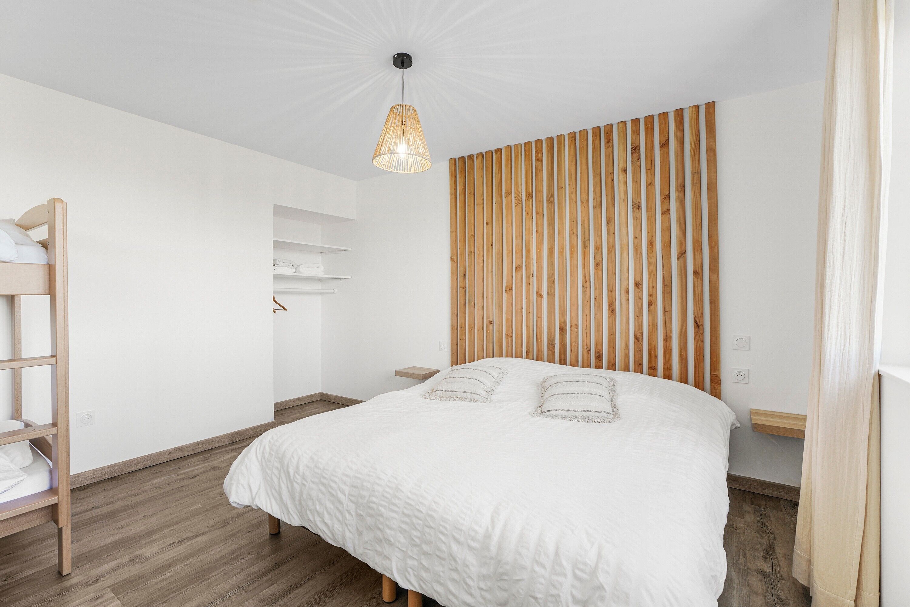 Une chambre avec un lit, un mur revêtu de lambris en bois, un luminaire suspendu et une échelle en bois.