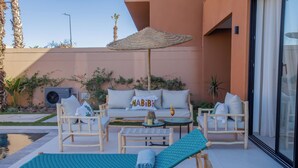 Uma área à beira da piscina com espreguiçadeiras, um conjunto de sofás e uma mesa com uma bebida.