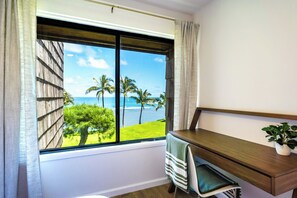 Een kamer met een groot raam met uitzicht op palmbomen en de zee.