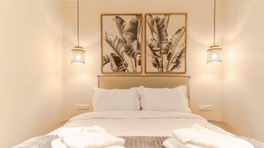 Una cama bien tendida con sábanas blancas y dos almohadas, un tapete texturizado y dos láminas enmarcadas con motivos botánicos en la pared.