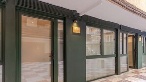Una hilera de puertas de vidrio con marcos verdes y un pequeño letrero iluminado sobre cada una.