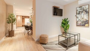 Una sala de estar moderna con piso de madera, una mesa de centro de vidrio, un sofá y un área de comedor al fondo.