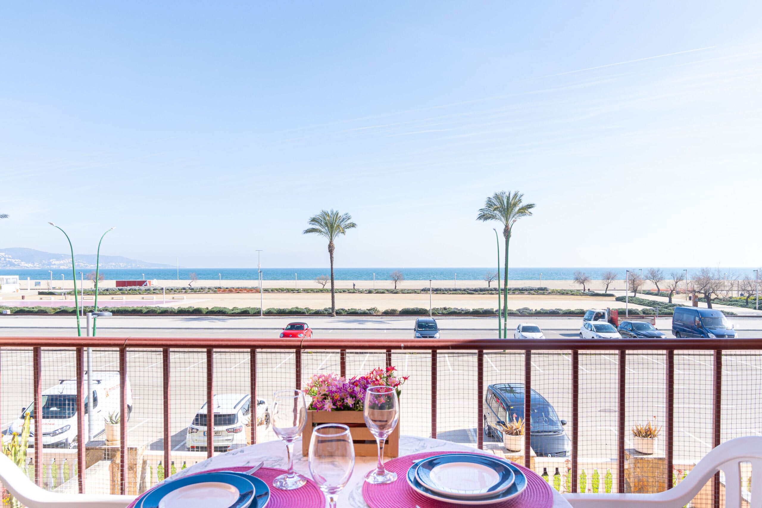 Une table de balcon avec vue sur la plage et les voitures garées.
