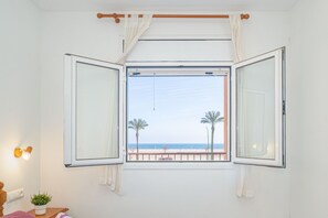 A room with a large window offering a view of the beach, palm trees, and the sea.