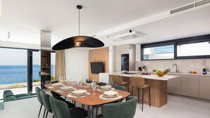 Een moderne keuken met een groot eiland, een eetgedeelte met groene stoelen en uitzicht op de zee.