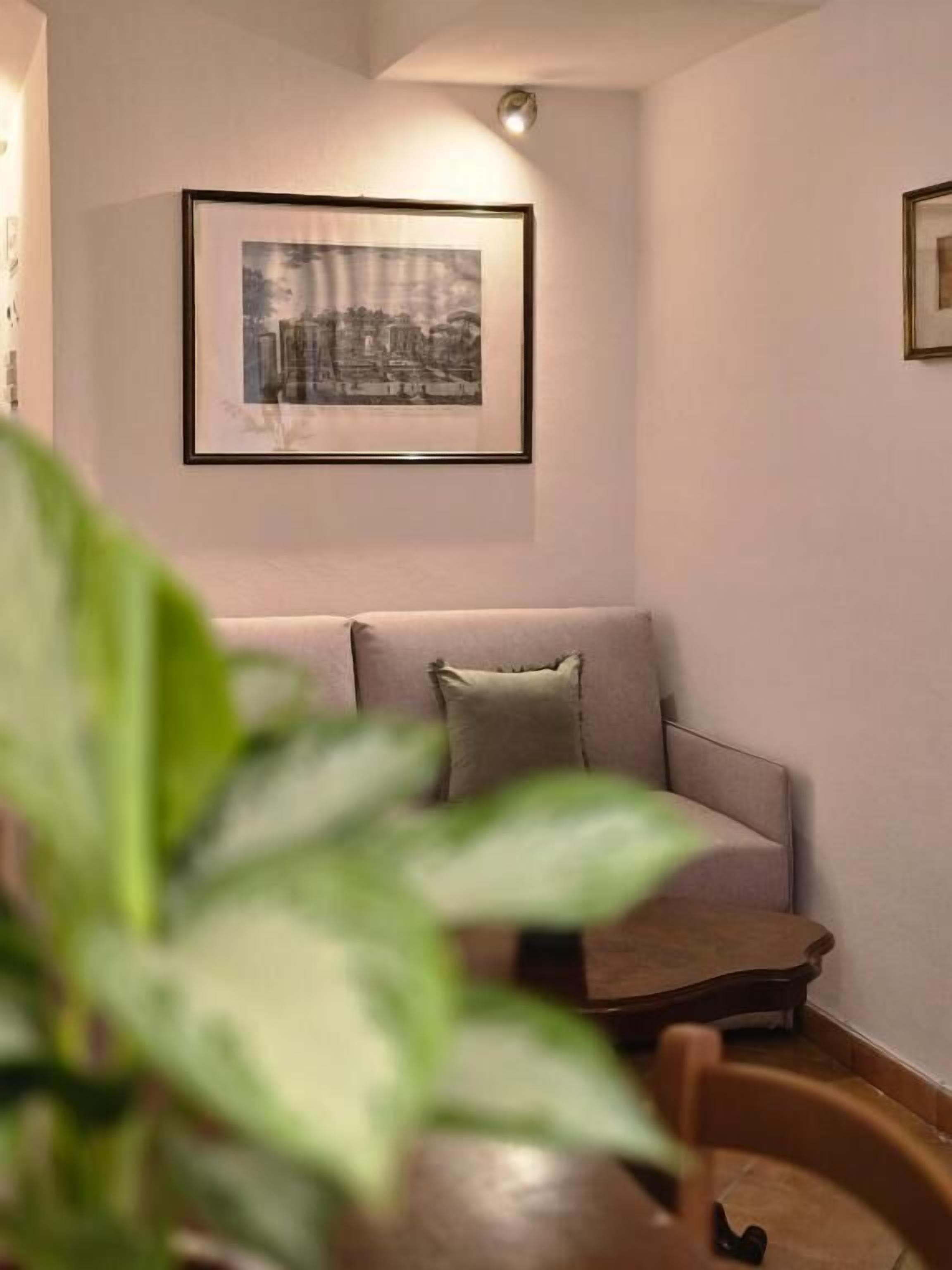 A cozy living room with a sofa, a framed picture on the wall, and a potted plant in the foreground.