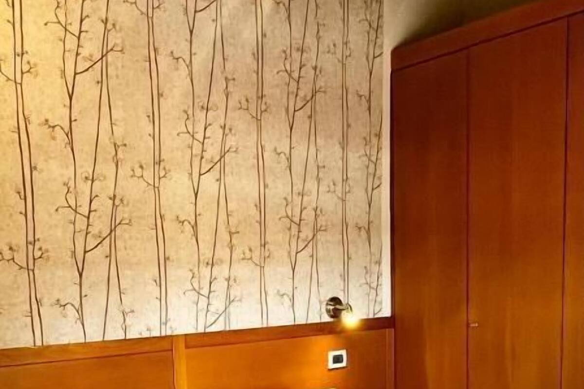 A hotel room with a large bed, wooden headboard, and a wall with a tree pattern.